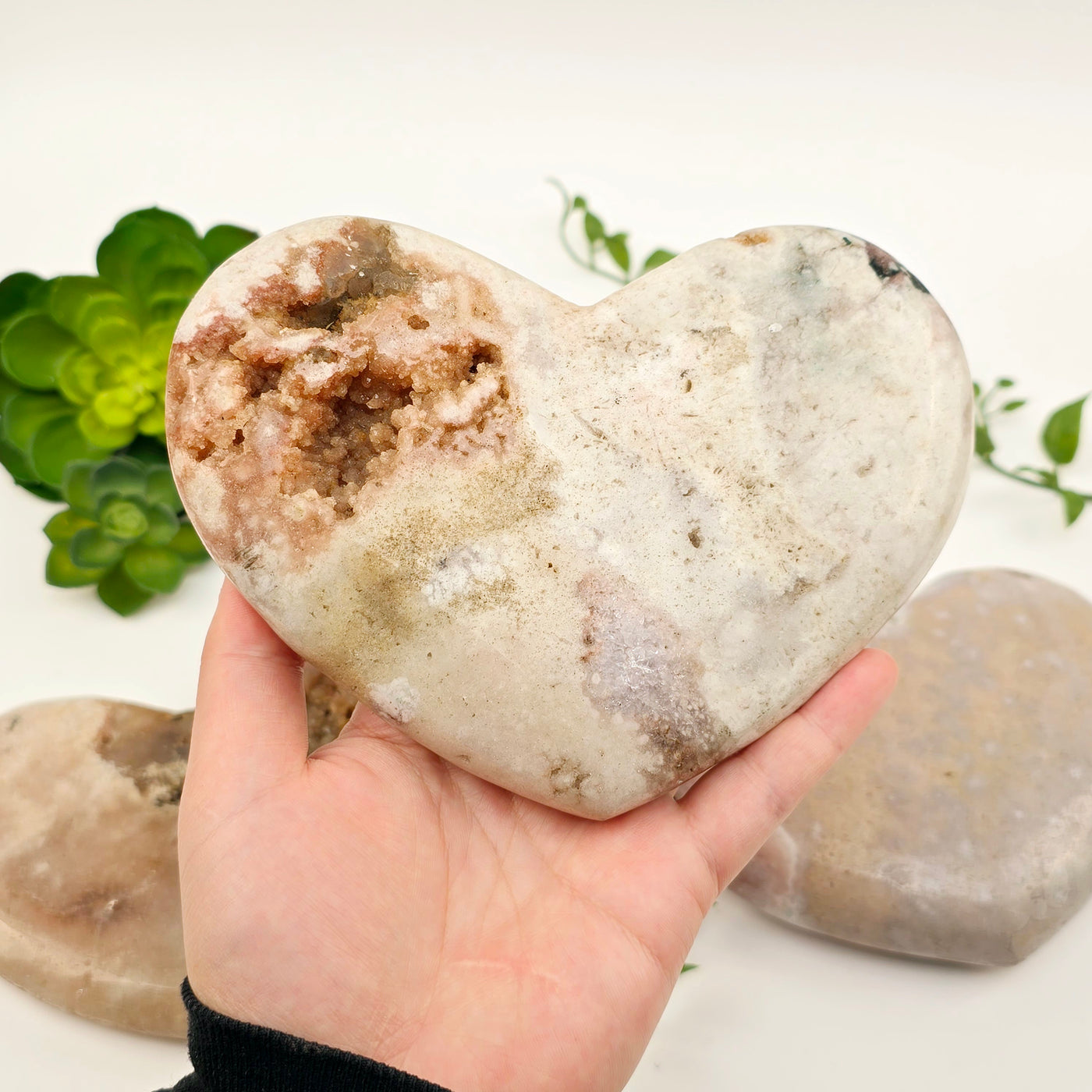 Pink Amethyst Polished Crystal Heart - You Choose #1 variant 2 in hand for size reference with other variants in the background with plants