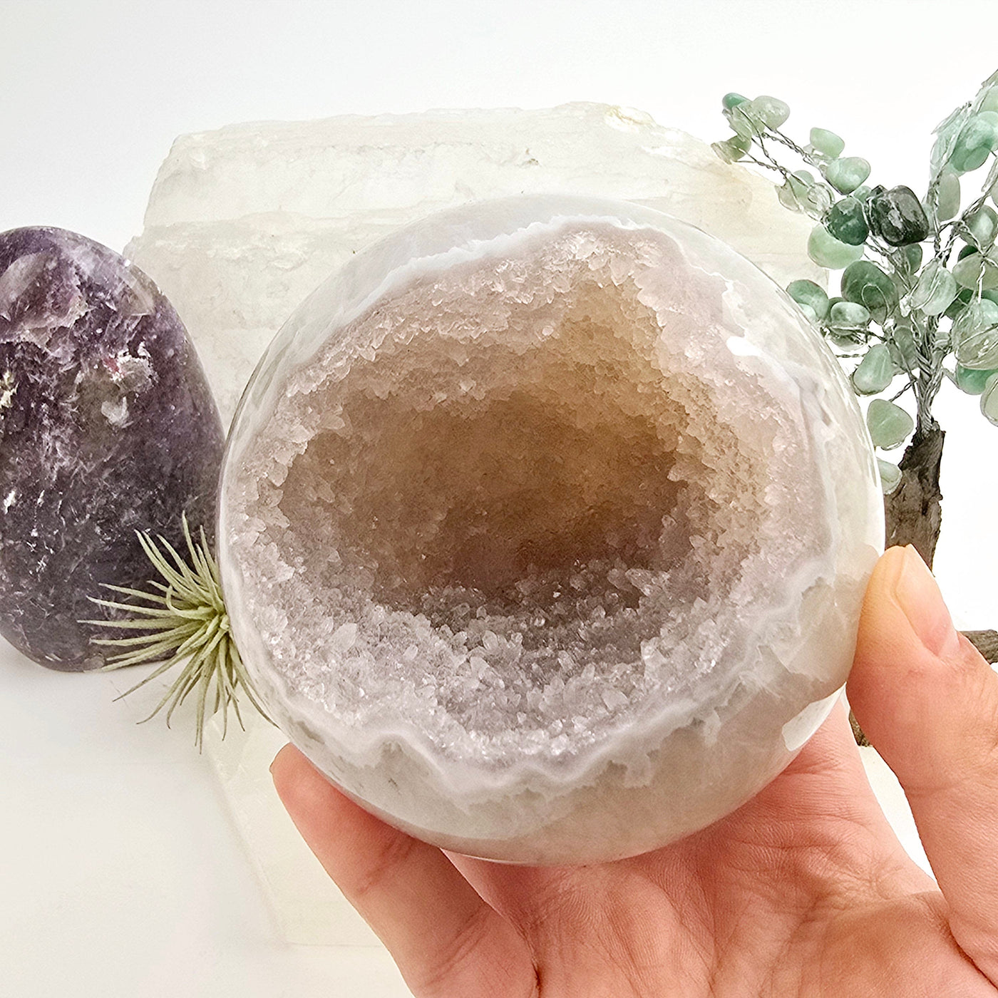 Amethyst Crystal Sphere One-of-a-Kind #7 in hand for size reference with props and plants in the background
