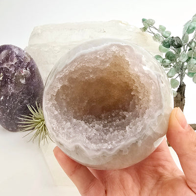 Amethyst Crystal Sphere One-of-a-Kind #7 in hand for size reference with props and plants in the background
