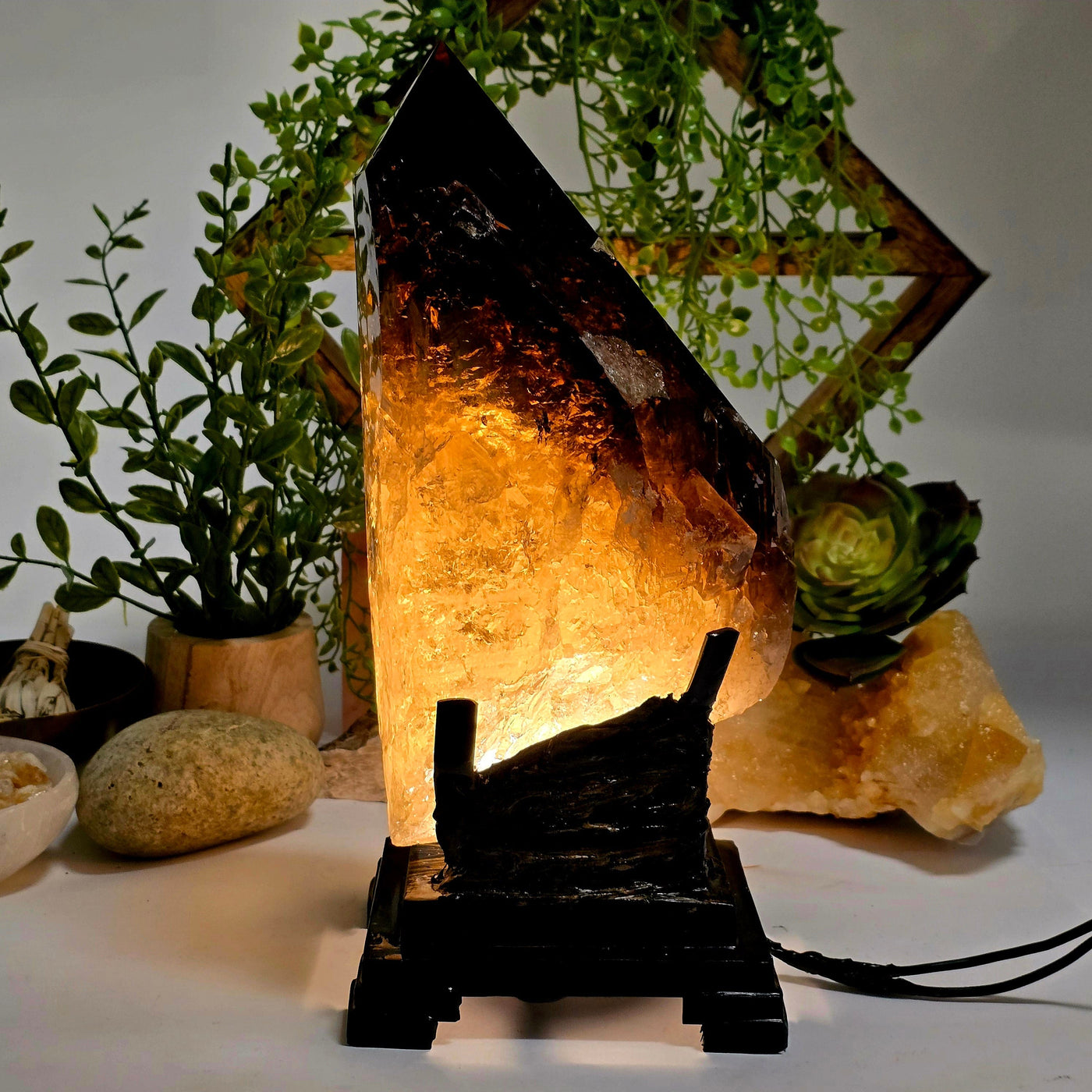 Natural Smokey Citrine Large Polished Crystal Point with Lamp on Stand - One-of-a-Kind #1 lamp lit up with dark background with props and plants
