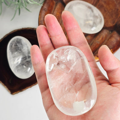 Crystal Quartz Palm Stone - You Choose variant 3 in hand for size reference with other variants in background with props and plants