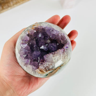 hand holding up amethyst sphere with decorations in the background