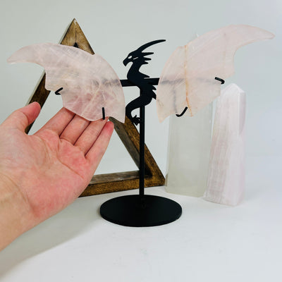 hand next to rose quartz dragon on metal stand with decorations in the background