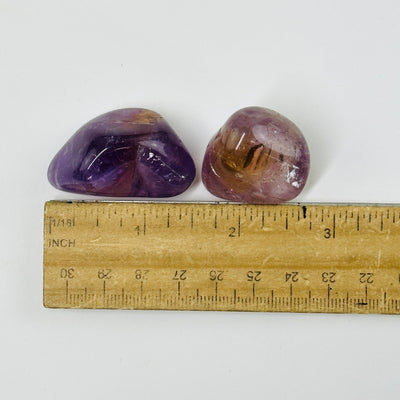 amethyst tumbled stones next to a ruler for size reference