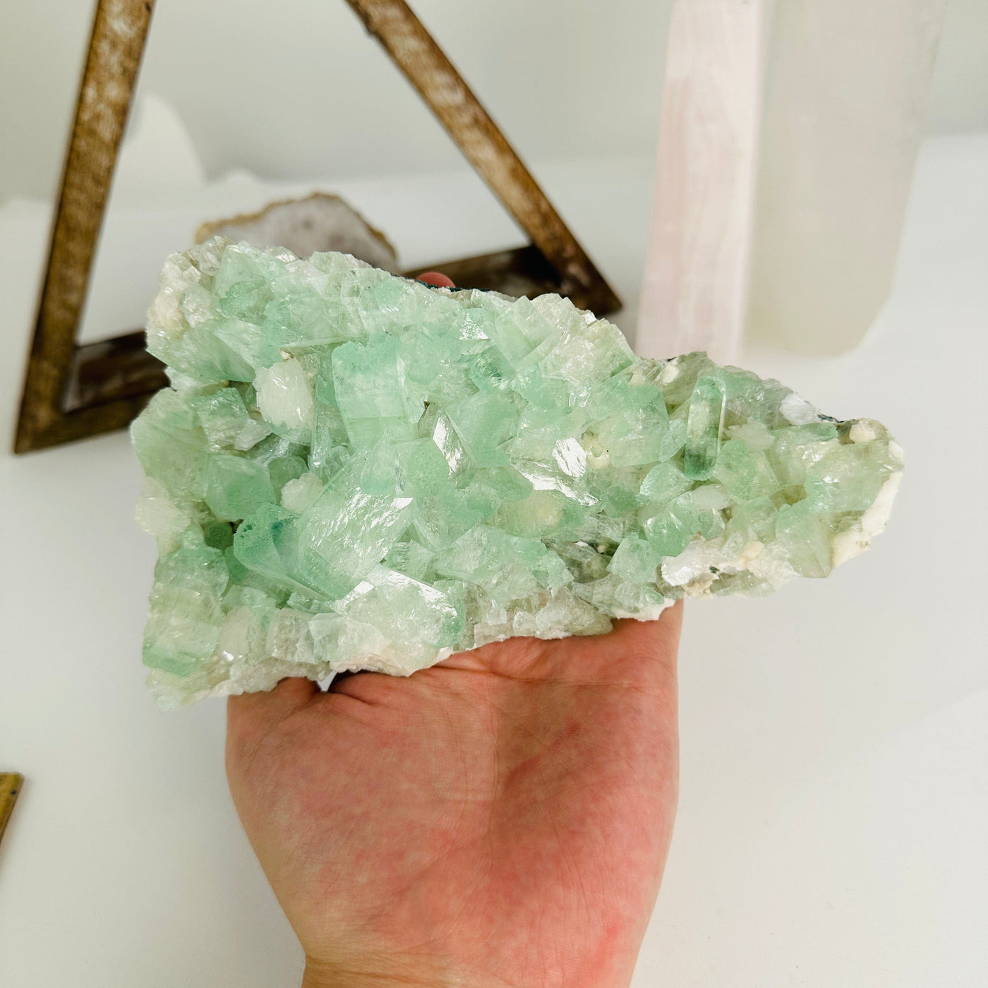 hand holding up green apophyllite on matrix with decorations in the background