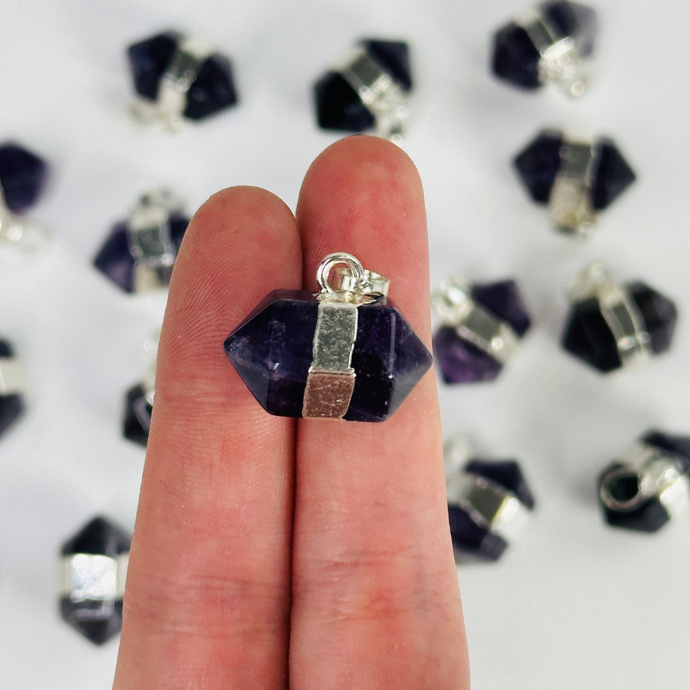 fingers holding up amethyst pendant with others in the background