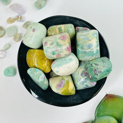 bowl filled with ruby fuchsite tumbled stones with decorations in the background