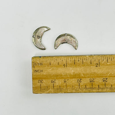 moon pendants next to a ruler for size reference