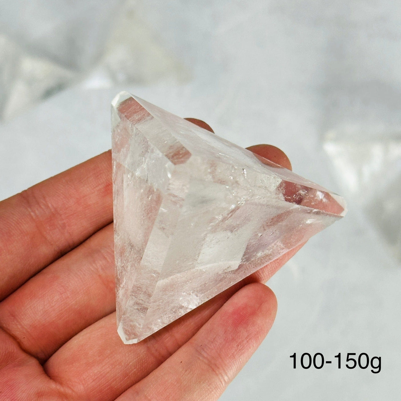 hand holding up 100-150g crystal quartz pyramid