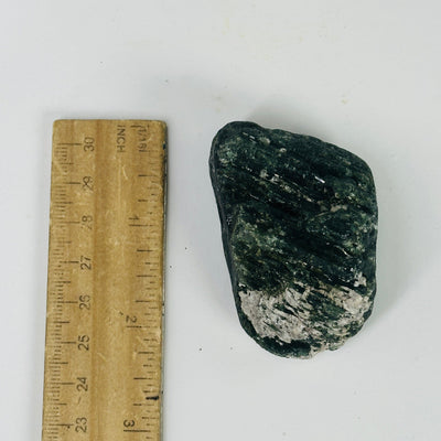 green and black tourmaline next to a ruler for size reference