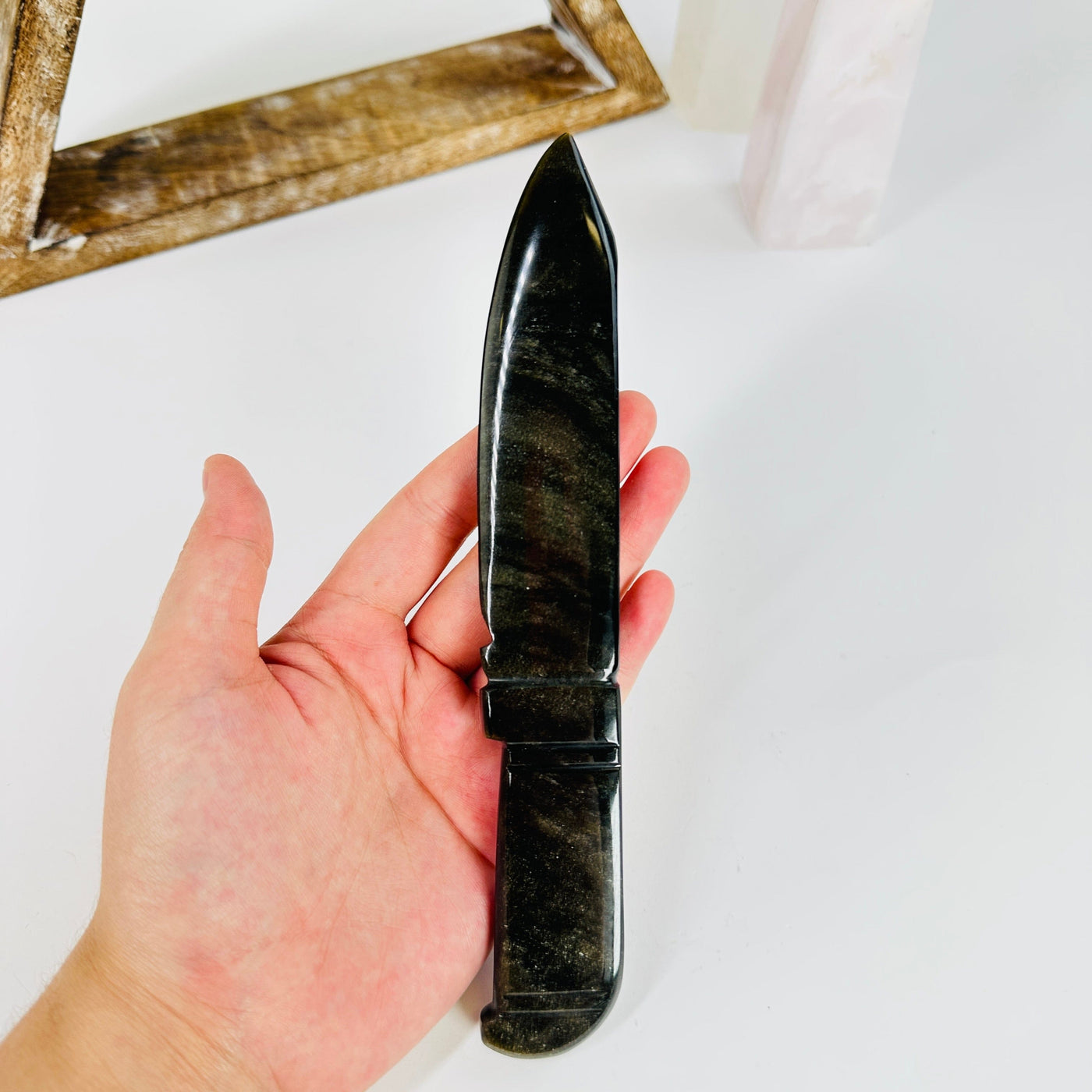 hand holding up obsidian knife with decorations in the background