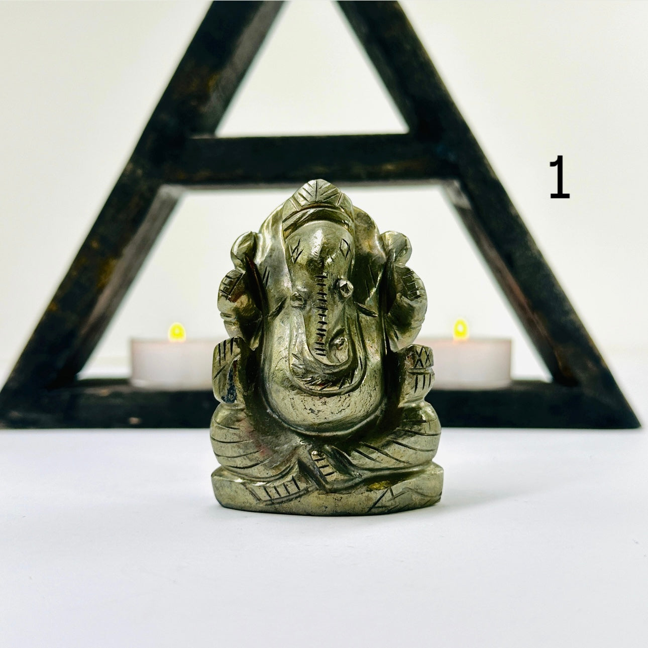 Pyrite Crystal Elephant Ganesha Carving variant 1 with a dark wood shelf and two small candled in the background.