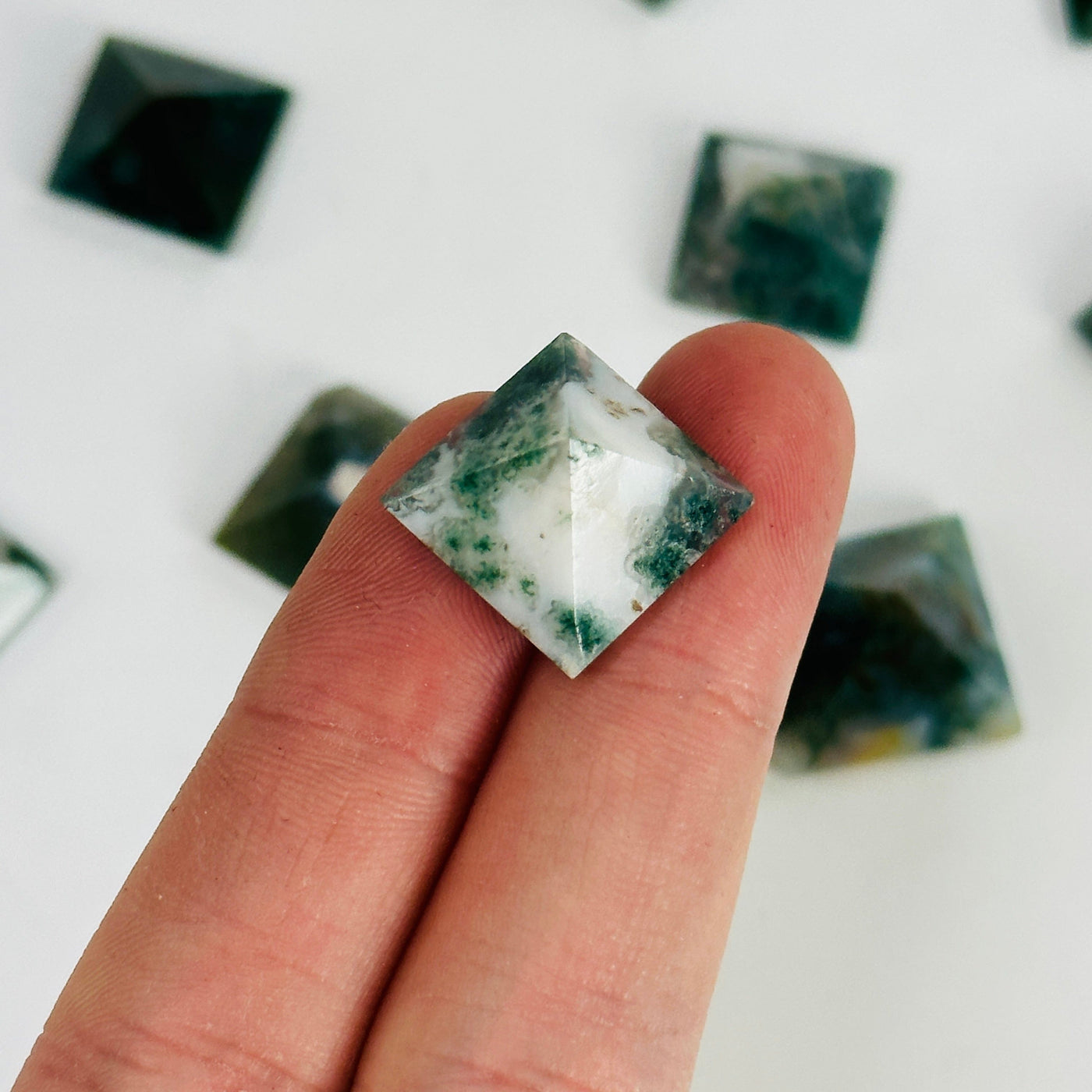 fingers holding up moss agate pyramid with others in the background