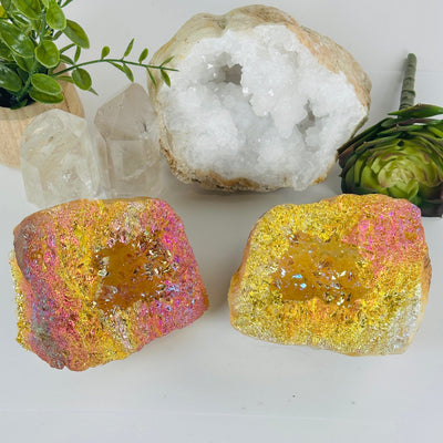 Sunshine Aura Quartz Crystal Geode Pair front view with props and plants in the background