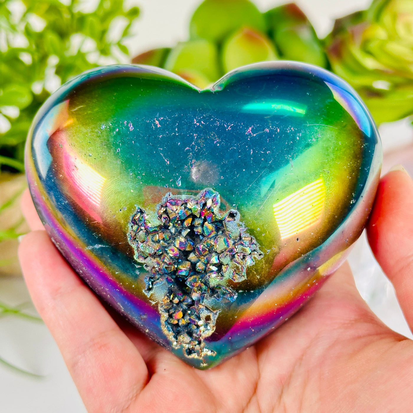 Rainbow Titanium Coated Crystal Heart - One-of-a-Kind in hand for size reference with props and plants in the background