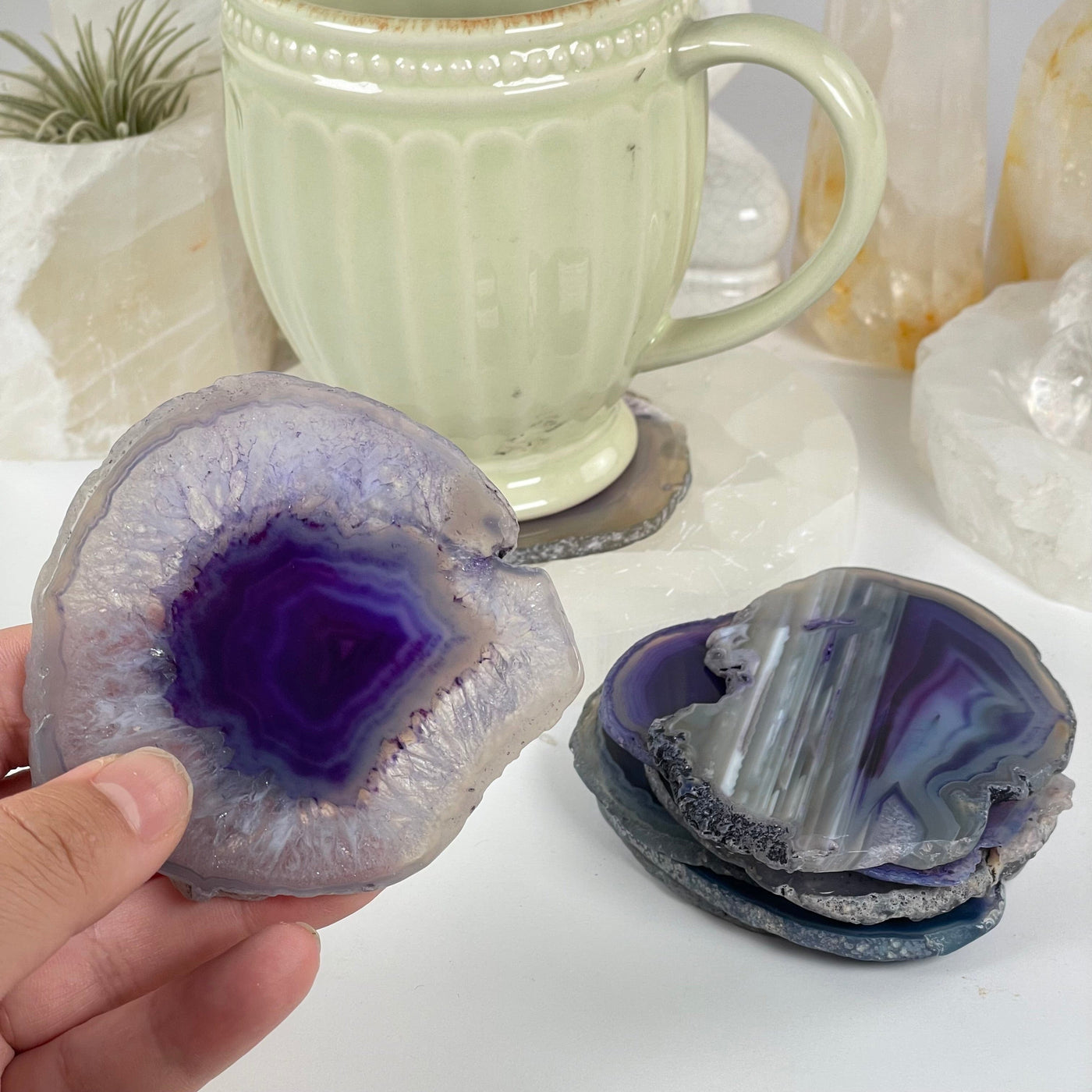 Purple Agate Slice Coasters Set - Set of 8 Small Coasters one in hand for size reference with others in the background in a stack next to one being used as a coaster for a cup