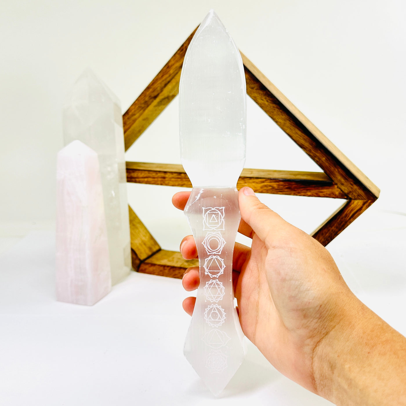  Etched Selenite Crystal Knife being held with a wood shelf and 2 crystal points in the background.