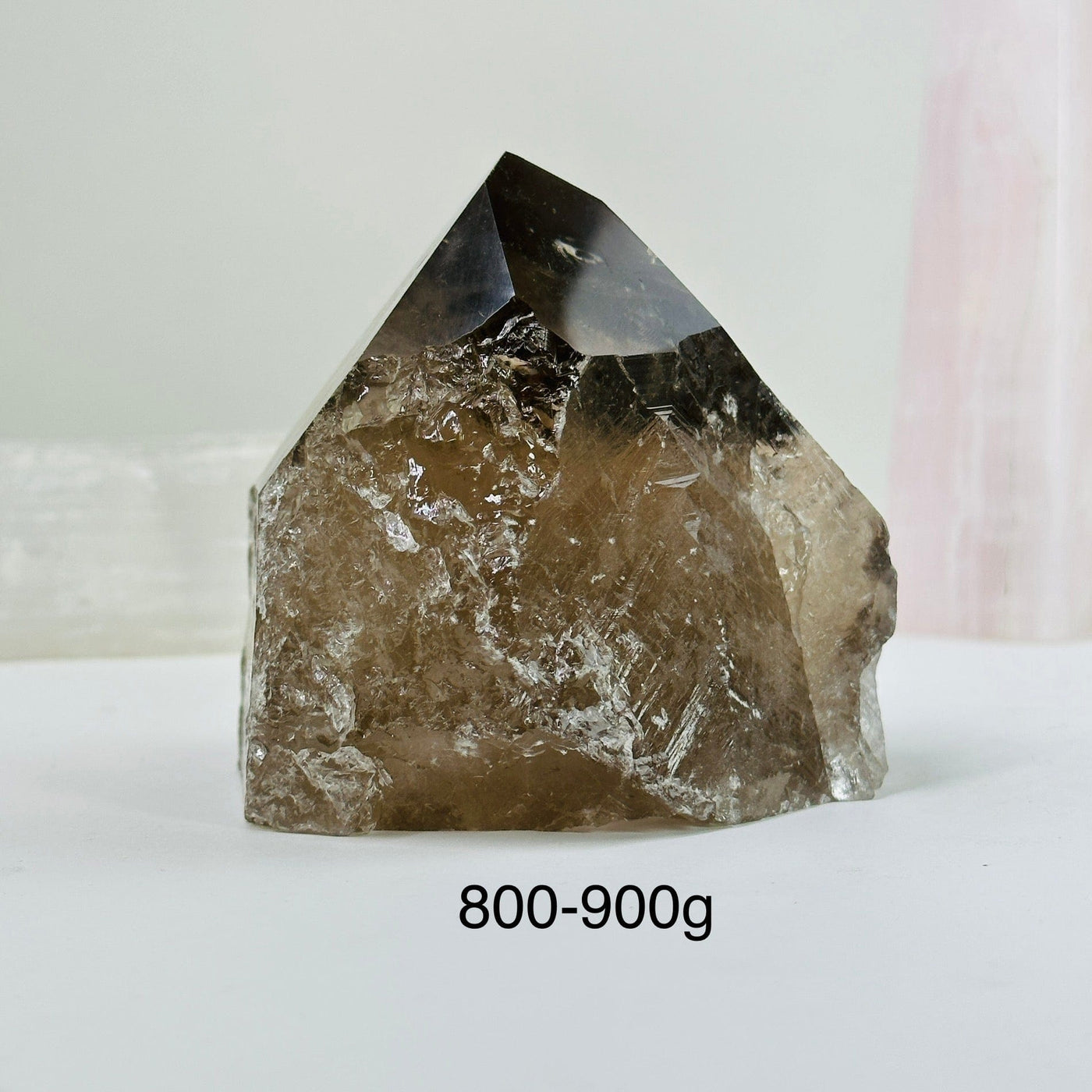 800-900g smoky quartz semi polished point with decorations in the background