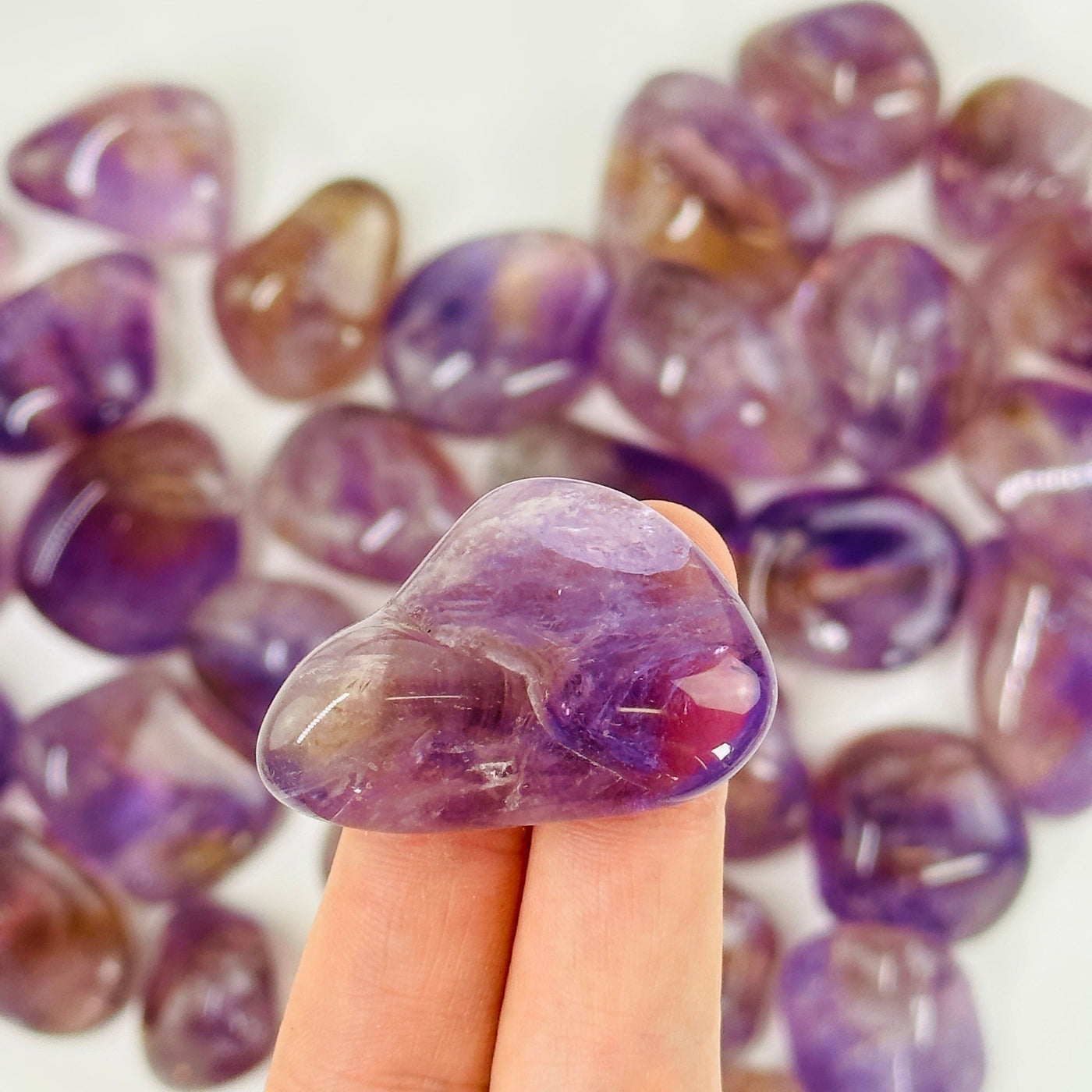 fingers holding up amethyst tumbled stone with others in the background