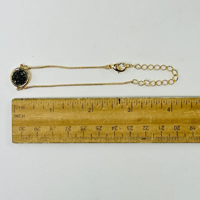 black diamond druzy gold snake chain bracelet next to a ruler for size reference