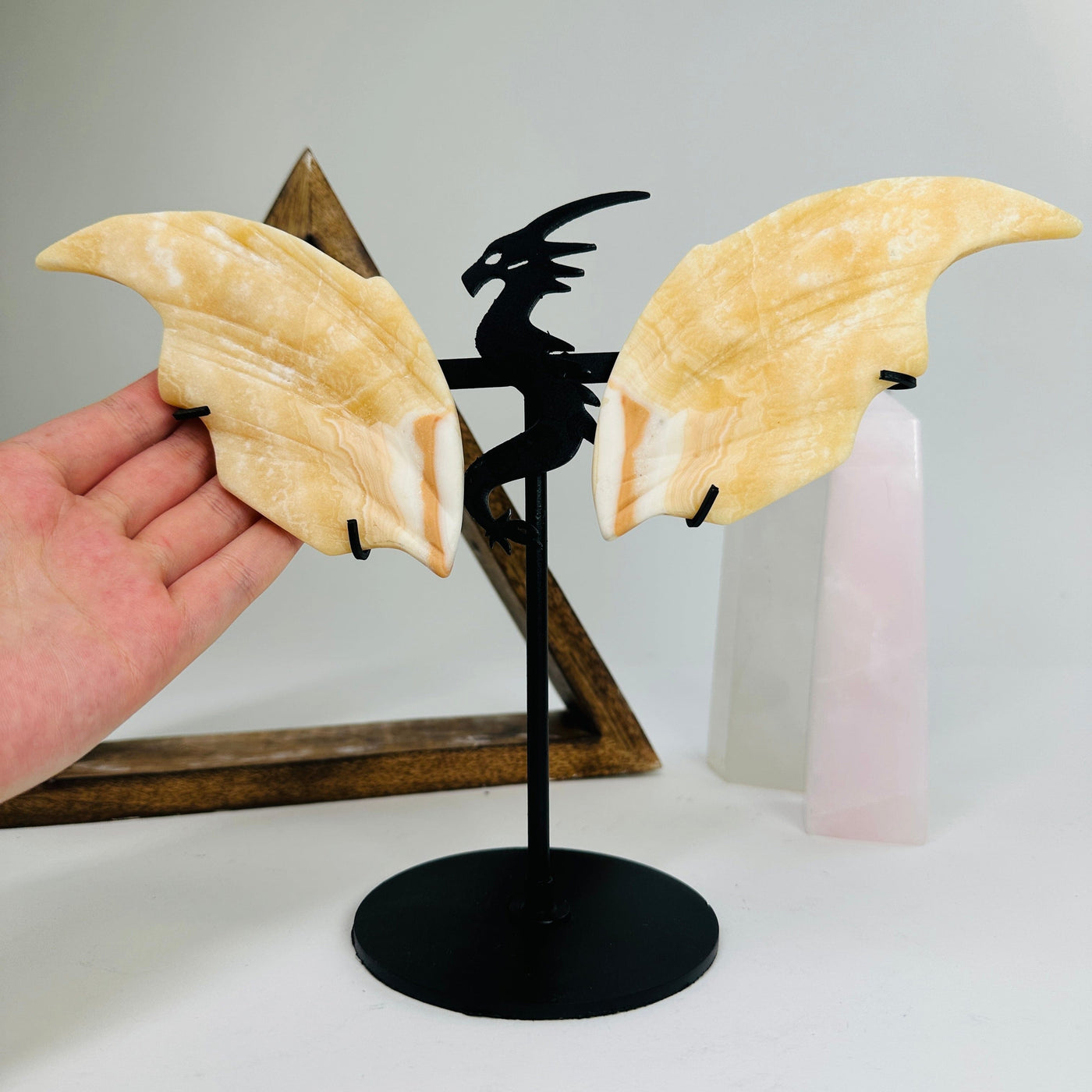 hand next to orange calcite dragon on metal stand with decorations in the background