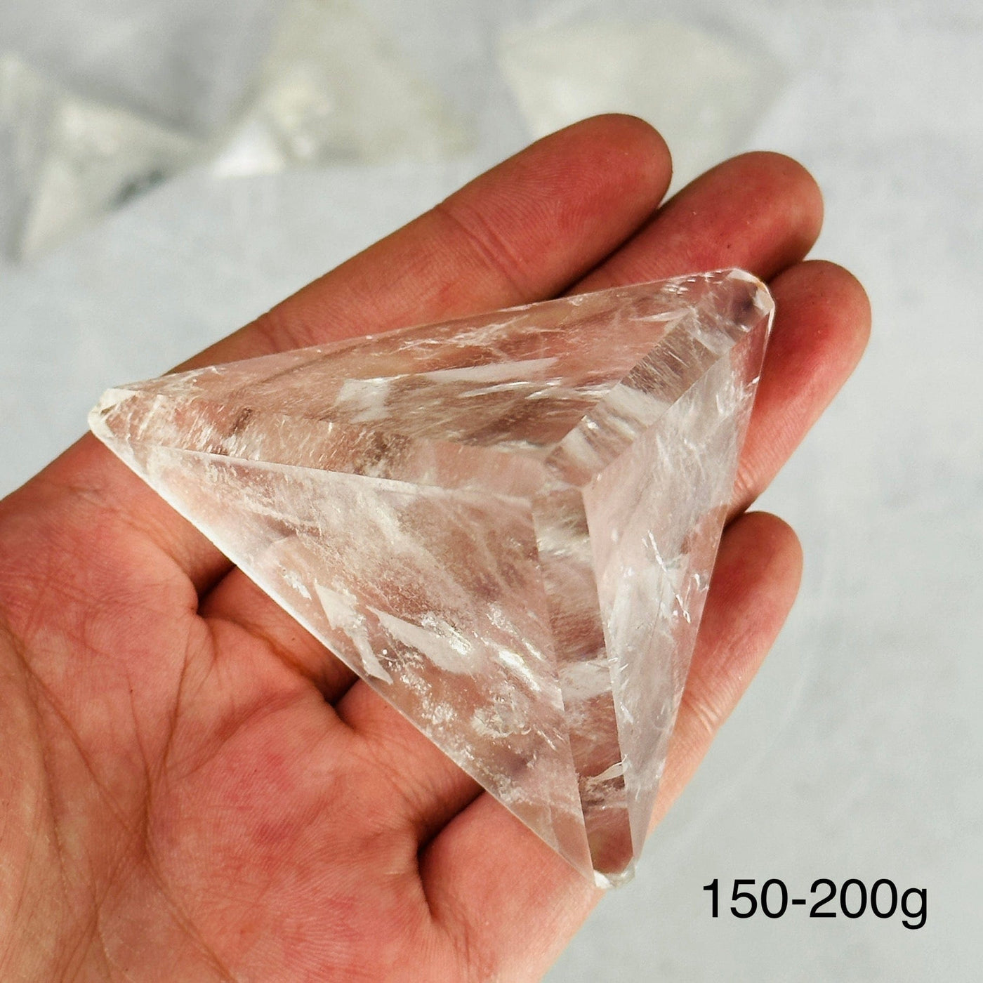 hand holding up 150-200g crystal quartz pyramid