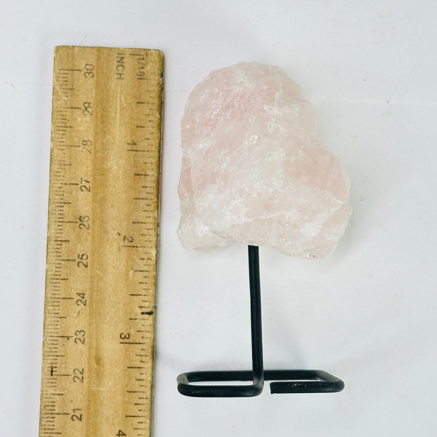Rose quartz on metal stand next to a ruler for size reference