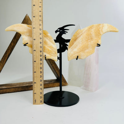 orange calcite dragon on metal stand next to a ruler for size reference