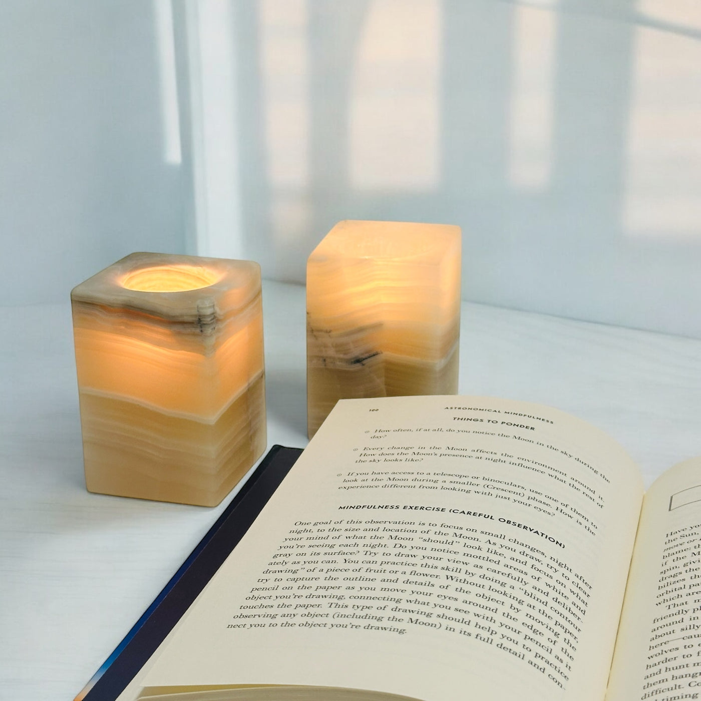 Mexican Onyx Crystal Candle Holders with a candle next to a book in a white room.