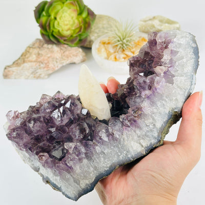 Amethyst Crystal Cluster with Calcite One-of-a-Kind #3 in hand for size reference with props and plants in the background