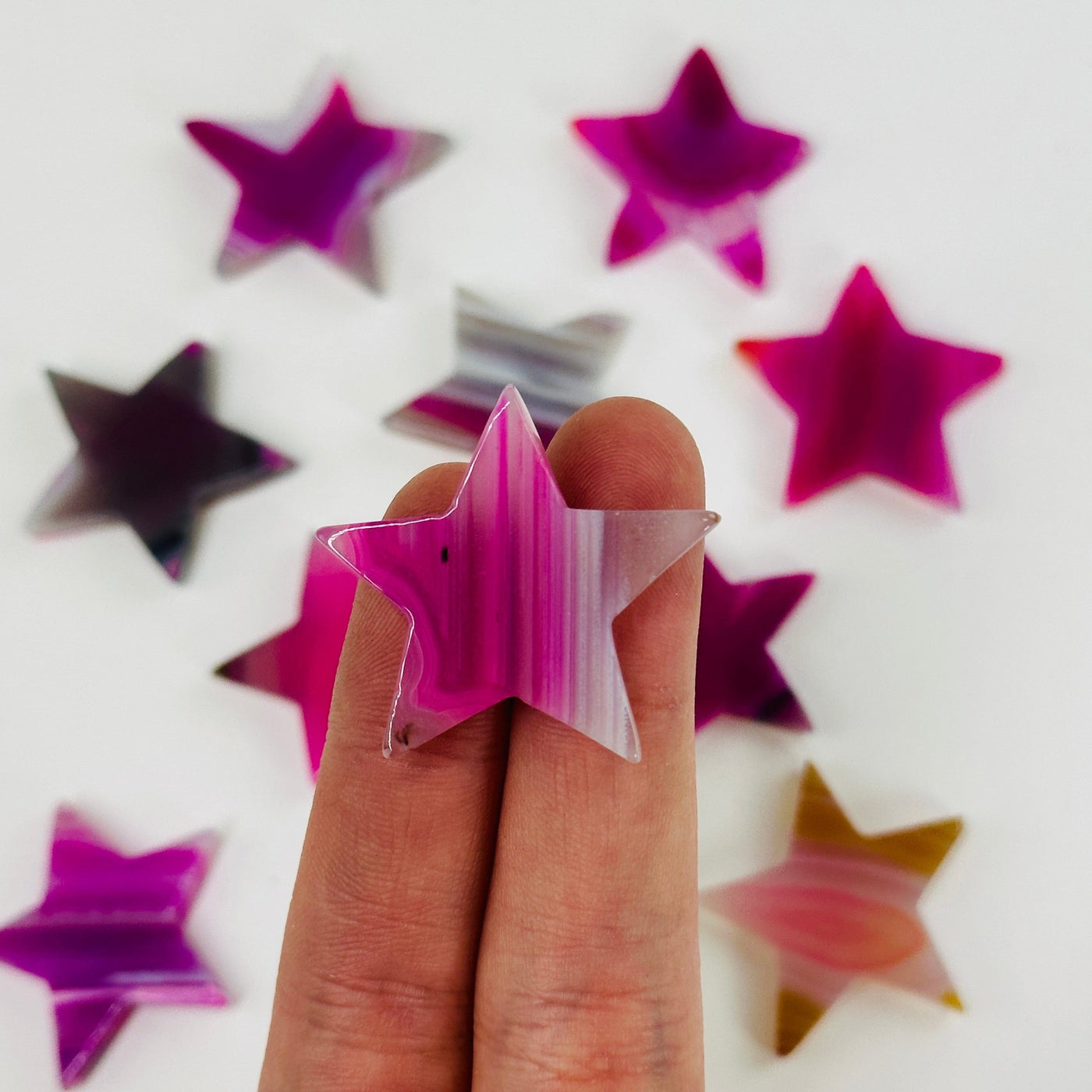 fingers holding up pink agate star with others in the background