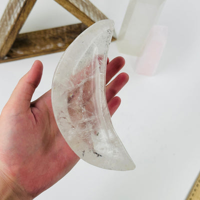 hand holding up crystal quartz moon bowl with decorations in the background