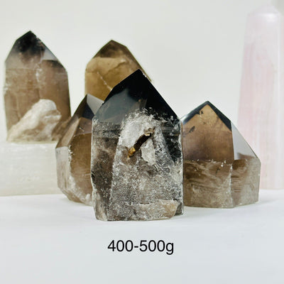 400-500g smoky quartz semi polished point with decorations in the background