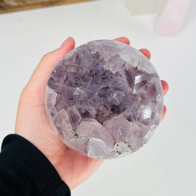 hand holding up amethyst sphere with decorations in the background