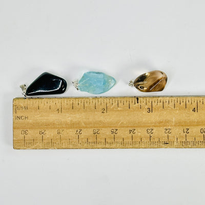 tumbled stone pendants next to a ruler for size reference