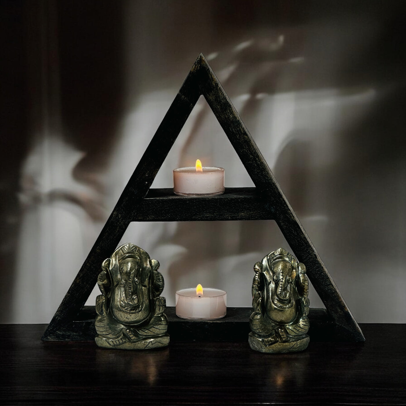 Pyrite Crystal Elephant Ganesha Carvings in front of a wood shelf with two small candles in a dark room.