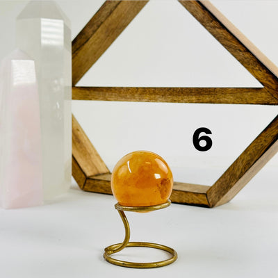 Golden Healer Crystal Sphere labeled variant 6 on a metal stand on a white table with a wood shelf and two crystal points in the background