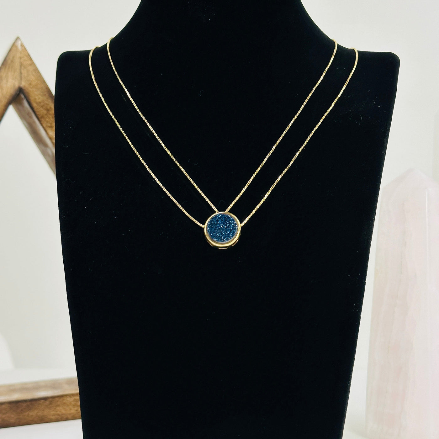 Mystic blue druzy double chain gold necklace with decorations in the background