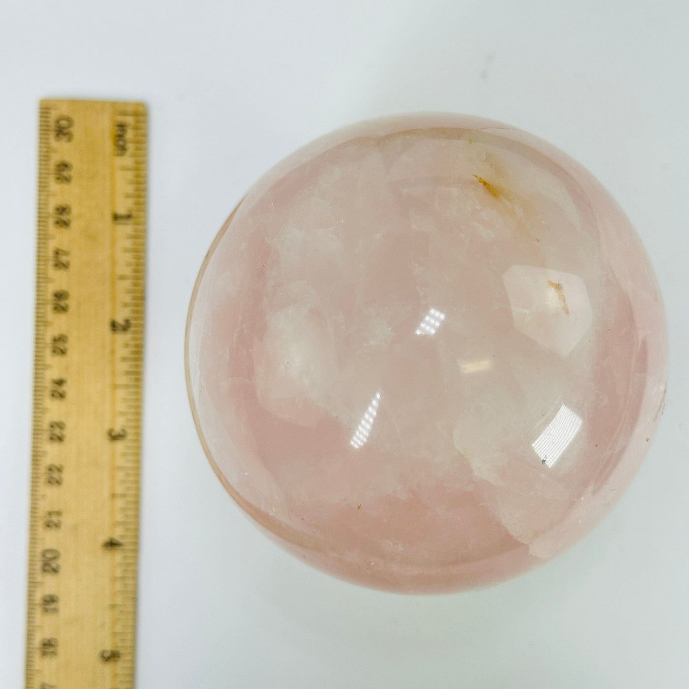 rose quartz sphere next to a ruler for size reference