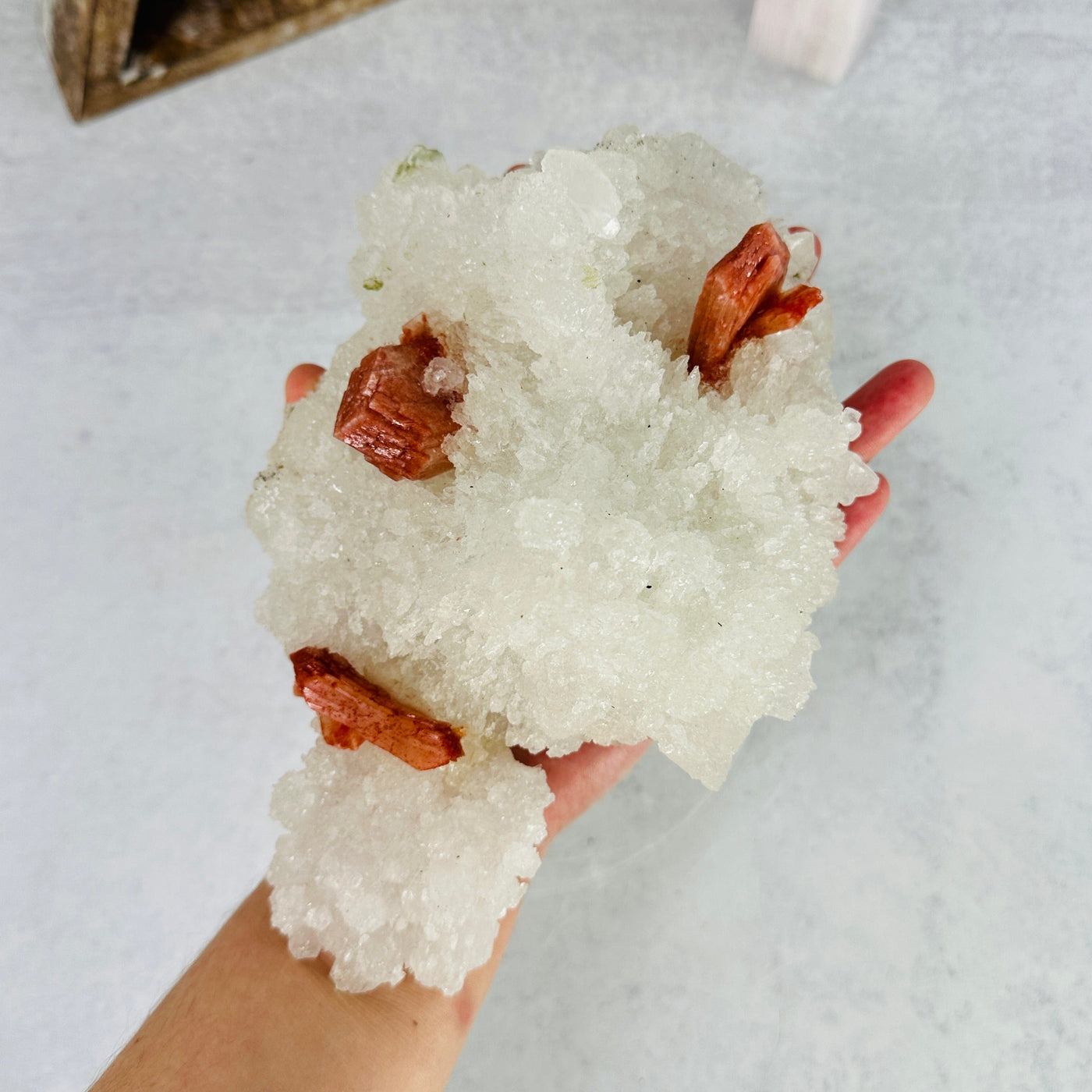 hand holding up apophyllite with stilbite cluster with decorations in the background