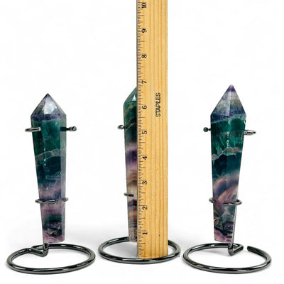 Three Rainbow Fluorite Crystal Wand Points on metal stands with a ruler for size refernce.