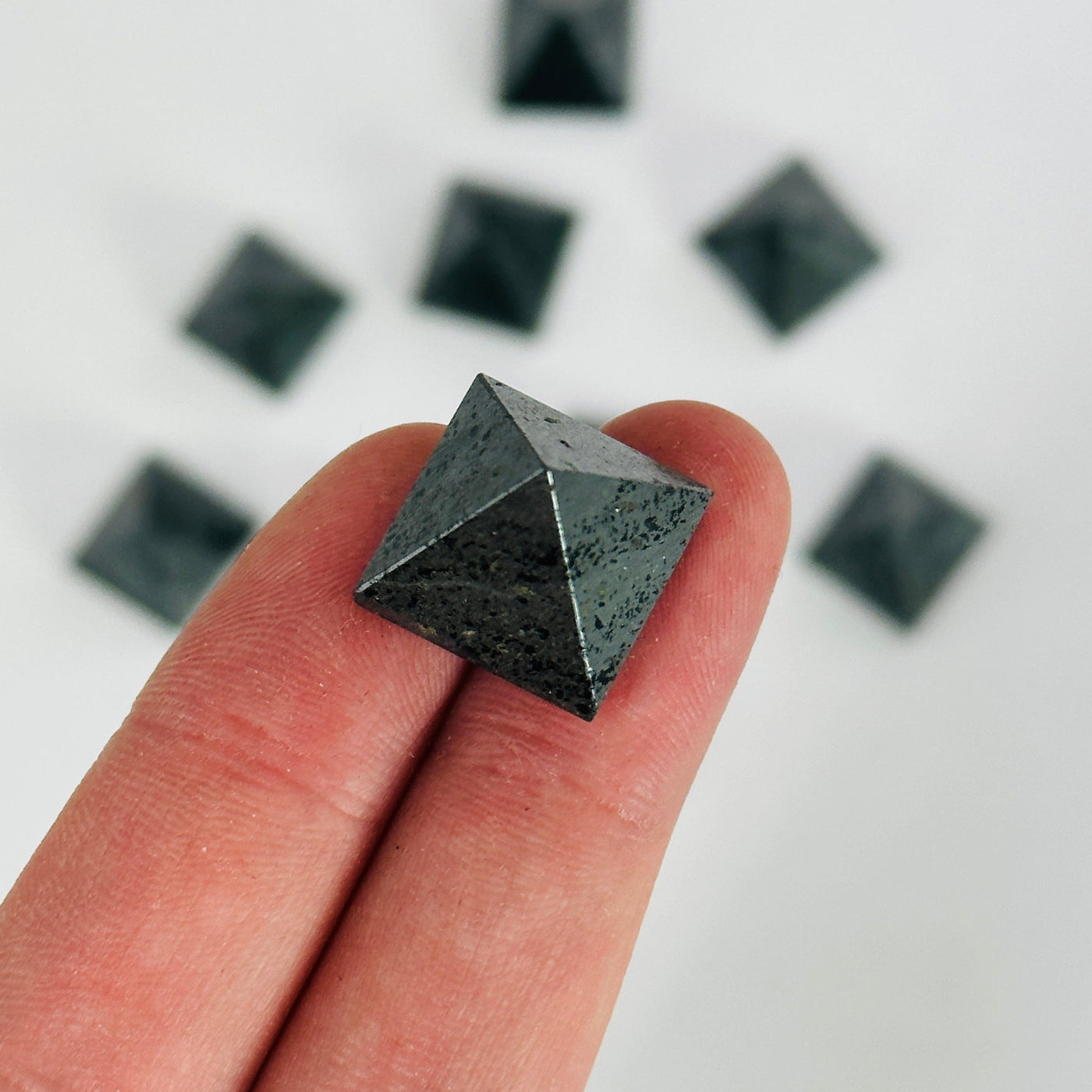 fingers holding up hematite pyramid with others in the background