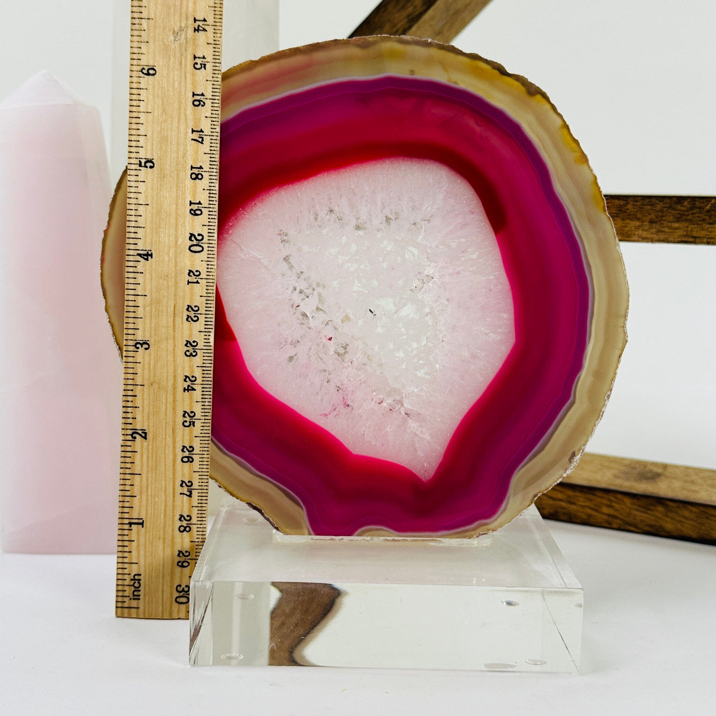 Pink agate slice on acrylic stand next to a ruler for size reference