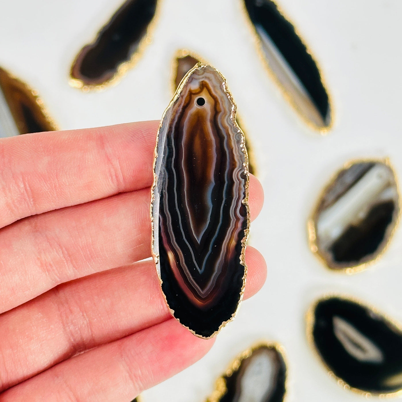 fingers holding up brown agate slice with others in the background
