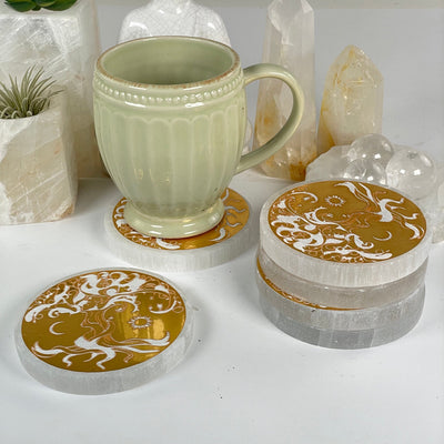Selenite Crystal Coasters with Gold Foil Tree of Life Decal - You Get All some shown in stack one shown individually one shown being used as coaster with a cup on it