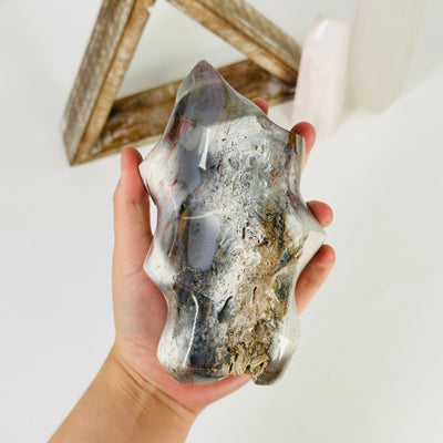 hand holding up ocean jasper flame point with decorations in the background