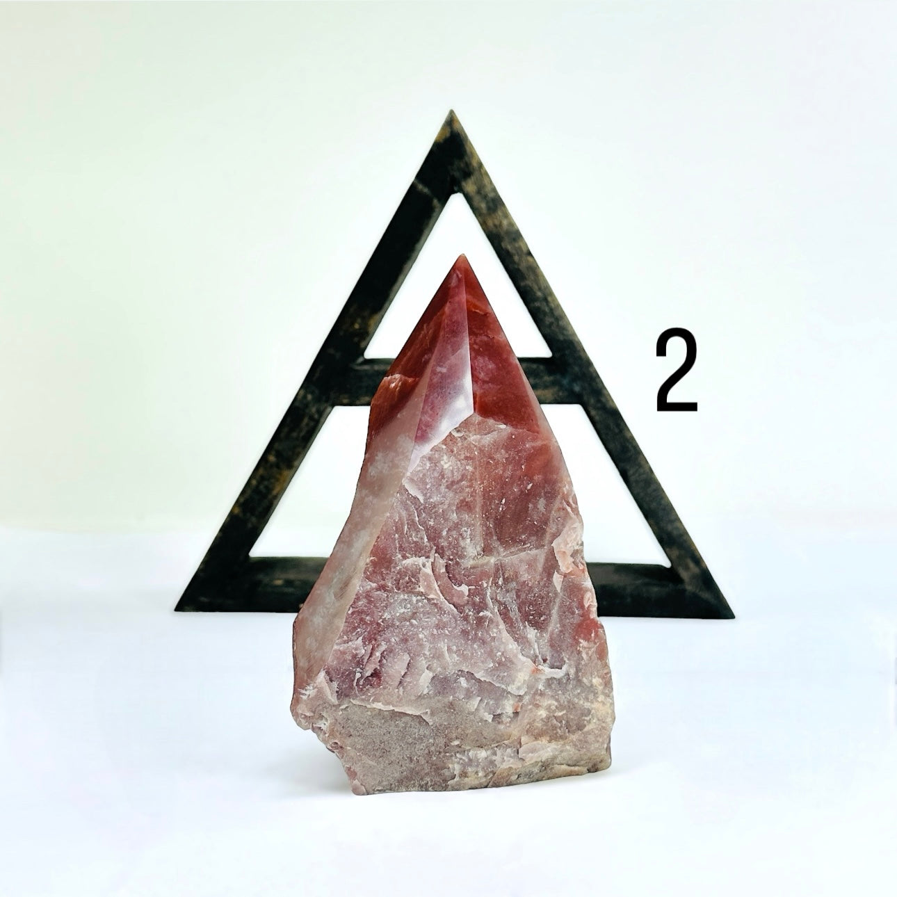 Guava Quartz Semi Polished Crystal Point variant two in front of  a wood shelf with a white background.