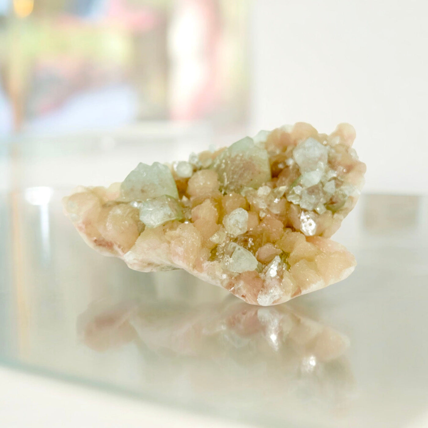 Peach Stilbite with Green Apophyllite - Zeolite Crystal Formation on glass surface with painting in the background