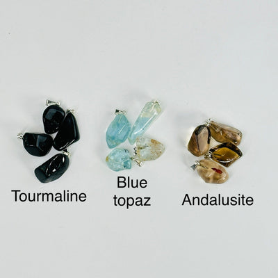 tourmaline, blue topaz, andalusite tumbled stone pendants on white background