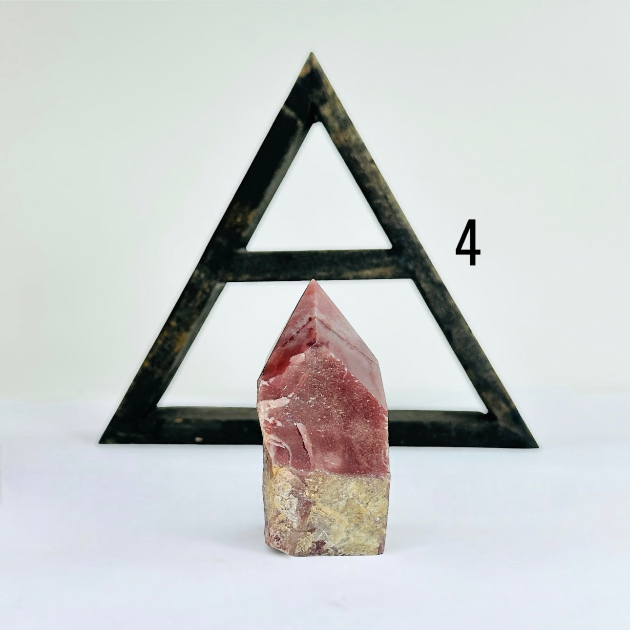 Guava Quartz Semi Polished Crystal Point variant four in front of  a wood shelf with a white background.